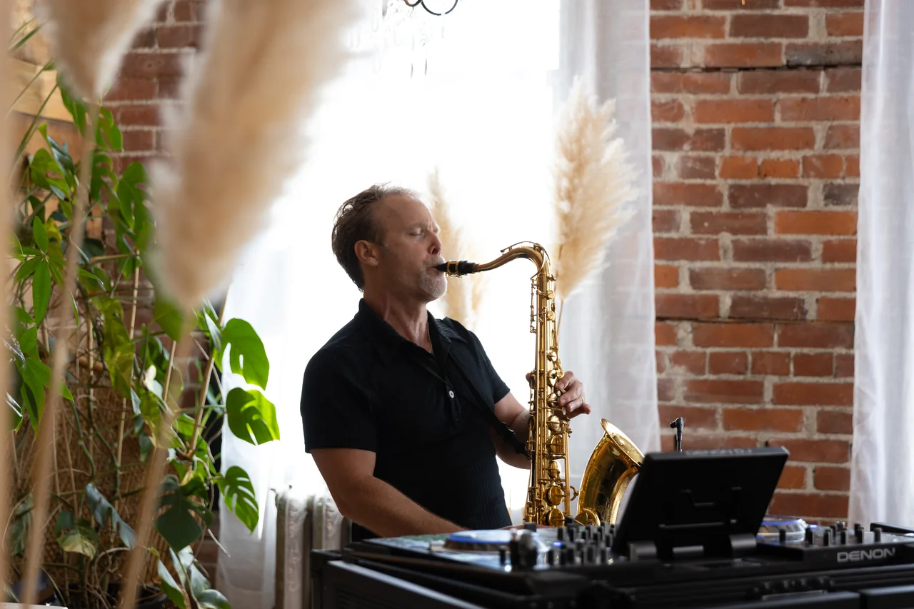 Howard Anderson performing saxophone beside a DJ controller